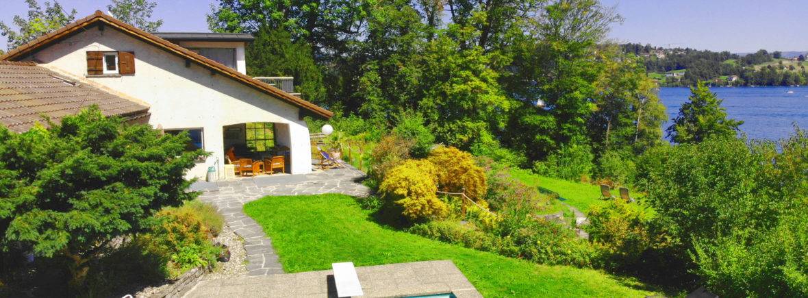 Experience the serene blend of luxury and nature at Classic Lakeside Villa Lucerne, nestled against the stunning backdrop of the Swiss Alps. This image captures the villa's majestic charm, its inviting infinity pool, and the pristine waters of Lake Lucerne, offering guests a picturesque retreat.